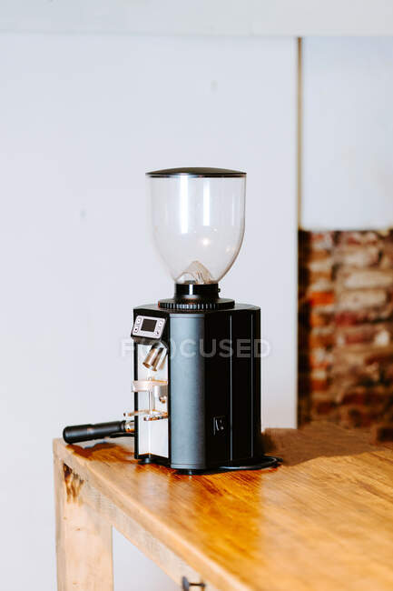 Contemporary coffee grinder placed on wooden counter in coffee shop with bright interior — Stock Photo