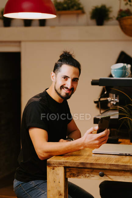 Side view happy barista browsing laptop while sitting at counter in coffee shop and working — Stock Photo