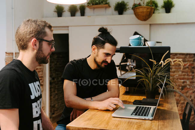 Male baristas sitting at counter with laptop in cafe and talking about work issues — Stock Photo