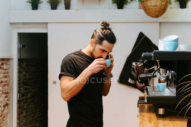 Focalisé mâle barista odeur expresso aromatique dans une petite tasse tout en travaillant dans un café — Photo de stock