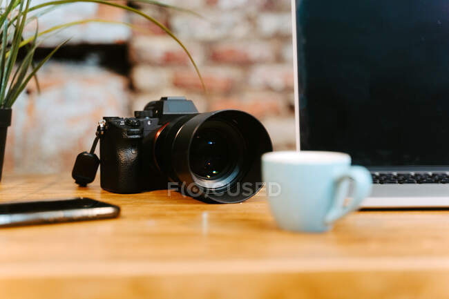 Workplace of freelancer with modern netbook and professional photo camera placed on wooden table with cups of espresso and notepad in cafe — Stock Photo