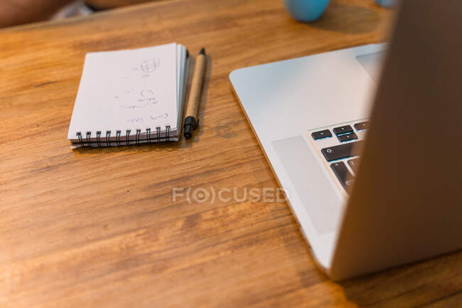 Local de trabalho de freelancer com netbook moderno colocado em mesa de madeira com xícaras de café expresso e bloco de notas no café — Fotografia de Stock