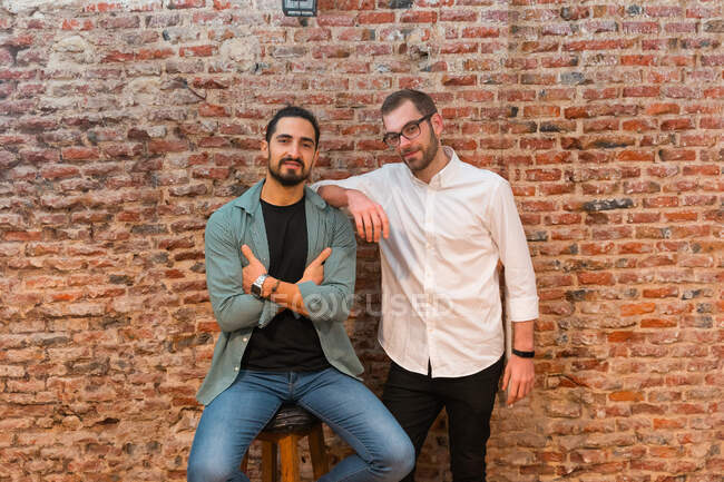 Smiling male baristas looking at camera on background of shabby brick wall in cafe in loft style — Stock Photo