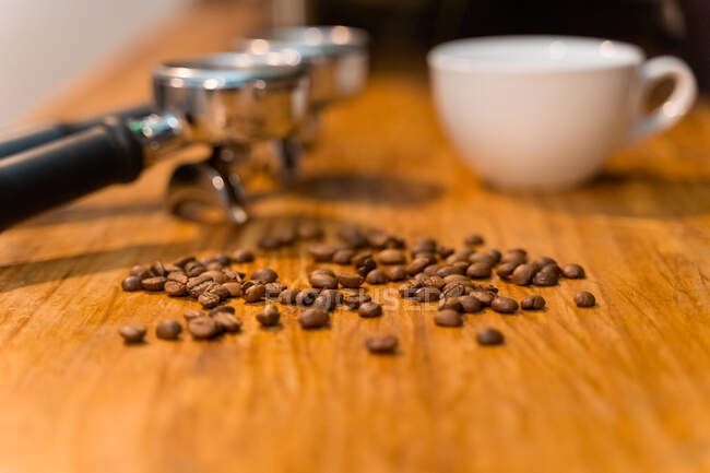 Portafilters placed on wooden table with empty cup and fresh coffee beans in cafe — Stock Photo