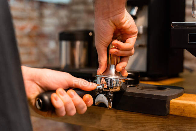 Crop unrecognizable barista pressing coffee in portafilter with tamper while preparing beverage in cafe — Stock Photo