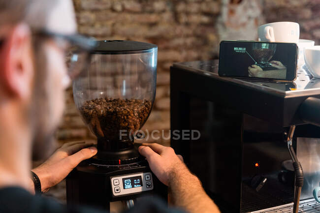 Чоловіча бариста використовує електричну шліфувальну машину і подрібнює кавові зерна під час роботи в кафе — стокове фото