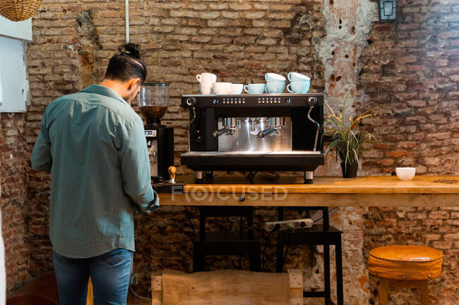 Voltar vista barista masculino usando portafilter e preparar café na cafeteira moderna, enquanto está em pé no balcão no café — Fotografia de Stock