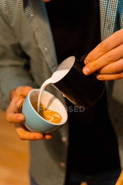 Alto angolo di coltura irriconoscibile barista aggiungendo latte in tazza con caffè mentre prepara gustoso cappuccino — Foto stock