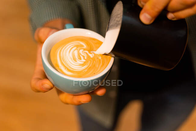 Высокий угол неузнаваемой баристы урожая добавляя молоко в чашку с кофе во время приготовления вкусного капучино — стоковое фото