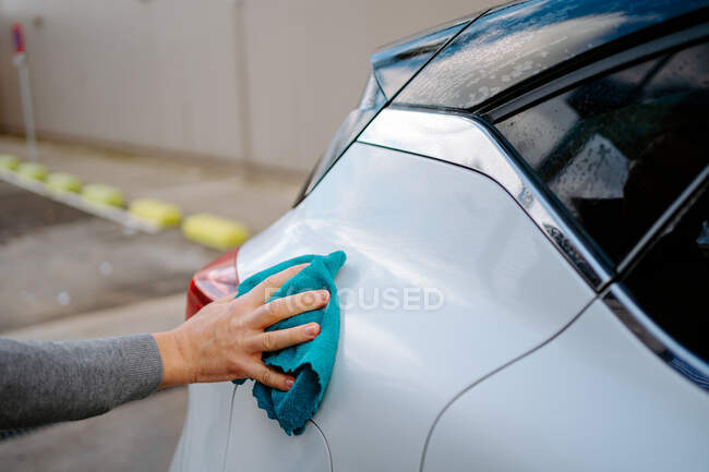 Cortado irreconhecível jovem macho limpando veículo com pano enquanto estava em pé na estação de lavagem de carro contra o céu nublado — Fotografia de Stock