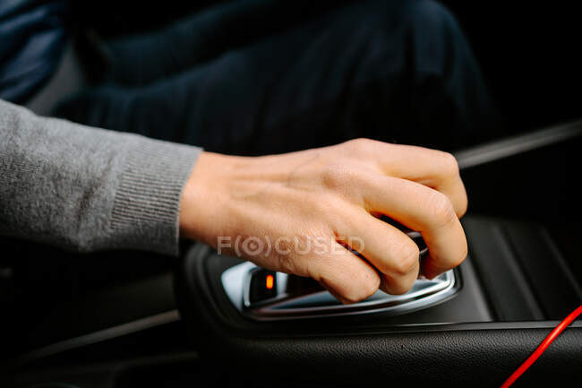 Зверху врожаю невизначений чоловік у повсякденному одязі з рукою на автоматичному спорядженні водіння сучасного автомобіля — стокове фото