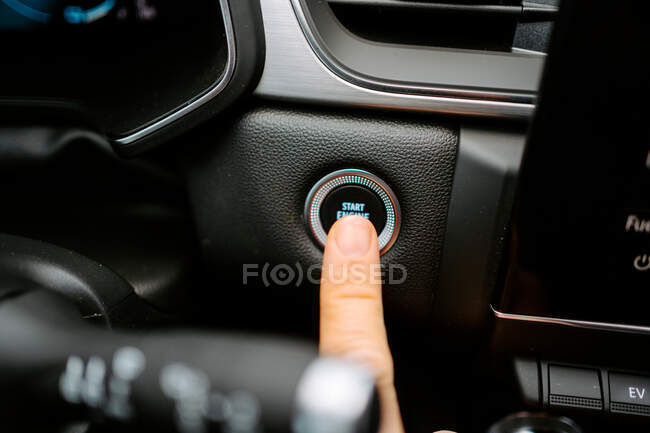 Primer plano de cultivo masculino anónimo pulsando el botón Start Engine Stop mientras está sentado en el coche moderno antes de conducir - foto de stock