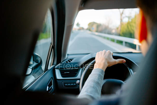 Back view of crop unrecognizable male driving a modern car on sunny day on motorway — Stock Photo