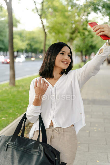 Delighted charming female standing on city street and taking self shot on smartphone during weekend stroll — Stock Photo