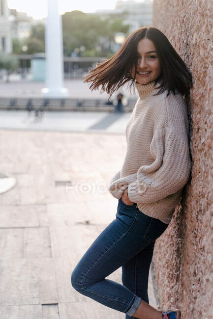 Side view of cheerful young female in casual outfit waving with hair on street and looking at camera — Stock Photo