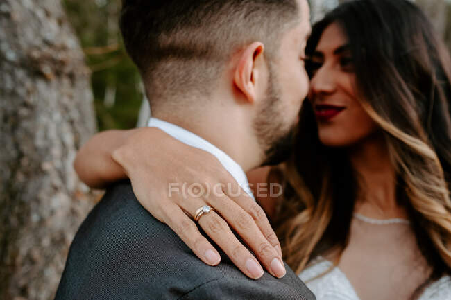 Young groom in elegant suit hugging forehead of graceful bride in white dress while standing in autumn forest on wedding day — Stock Photo
