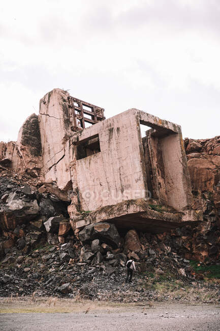 Кусок разрушенного цементного здания на открытой яме с грубыми камнями под облачным небом при дневном свете — стоковое фото
