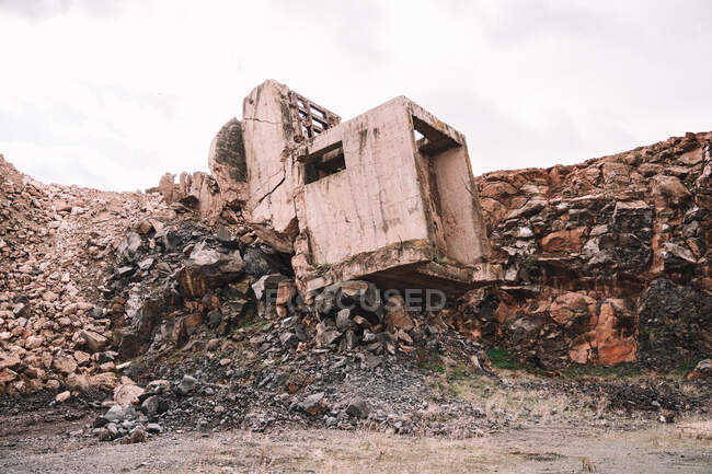Шматок зруйнованої цементної будівлі на відкритій ямі з грубими каменями під хмарним небом в денне світло — стокове фото