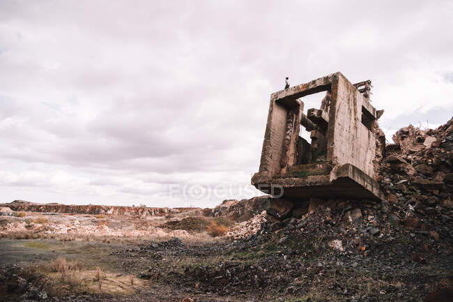 Piece of destroyed cement building on open pit with rough stones under cloudy sky in daylight — Stock Photo