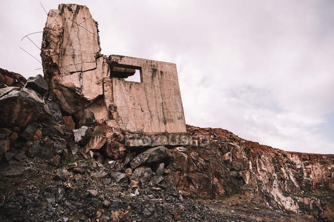 Pièce de ciment détruite à ciel ouvert avec des pierres brutes sous un ciel nuageux à la lumière du jour — Photo de stock