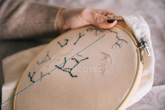 Side view of crop female with hoop and threads embroidering star constellations while sitting at table in light workshop — Stock Photo