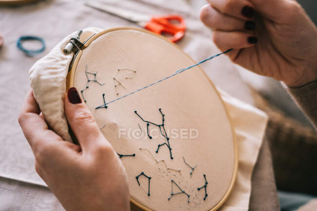 Side view of crop female with hoop and threads embroidering star constellations while sitting at table in light workshop — Stock Photo