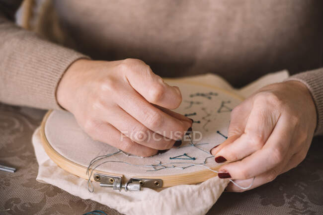Вид сбоку женщины с обручем и нитками, вышивающими звезду, сидя за столом в легкой мастерской — стоковое фото