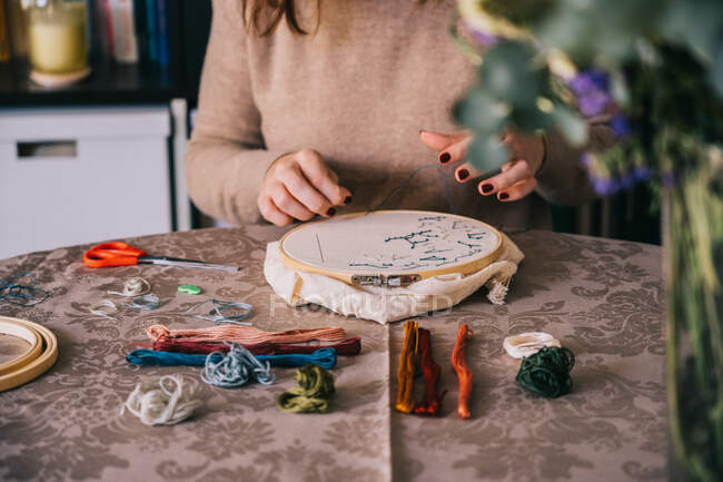 Front view of crop female with hoop and threads embroidering star constellations while sitting at table in light workshop — Stock Photo