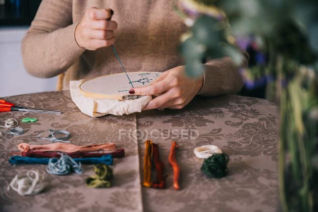 Vista frontal de la hembra de la cosecha con aros e hilos bordando constelaciones de estrellas mientras se sienta a la mesa en taller de luz - foto de stock