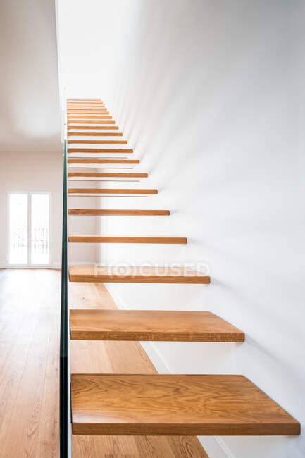 Scala in legno sopra parquet vicino alla parete bianca con ombra nell'edificio contemporaneo alla luce del giorno — Foto stock