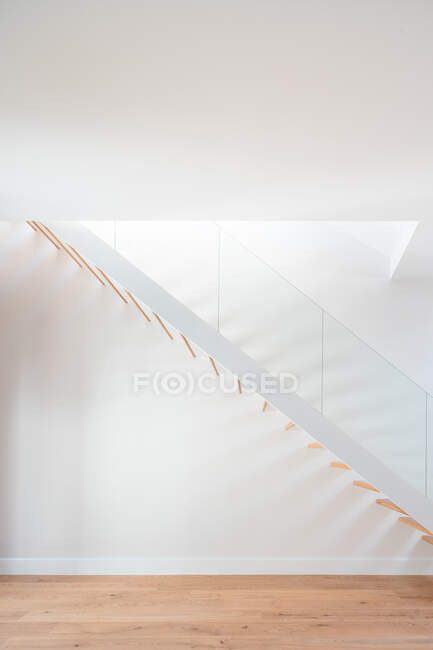 Escalier en bois au-dessus du parquet près du mur blanc avec ombre dans un bâtiment contemporain à la lumière du jour — Photo de stock