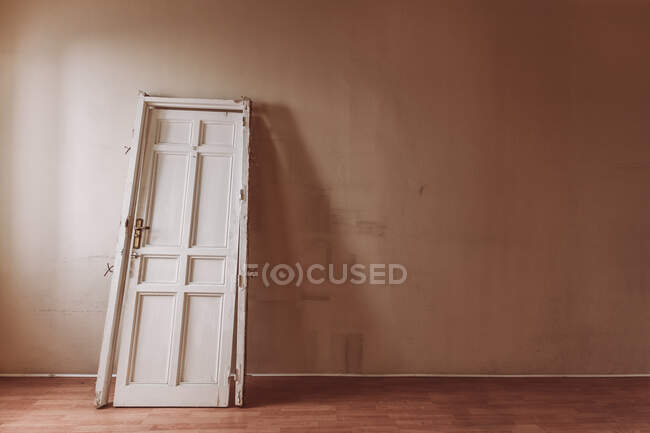 Porta de madeira branca com superfície rasgada colocada na velha sala vazia durante o dia — Fotografia de Stock