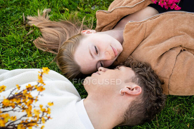 Giovane coppia che si guarda mentre riposa sull'erba con mazzi di fiori in fiore — Foto stock