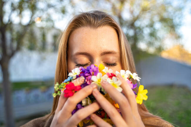 Анонімна молода ніжна жінка з закритими очима, що покриває обличчя барвистими квітами в місті — стокове фото