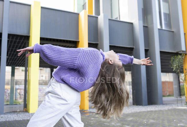 Side view fit pretty female wearing casual clothes bending backwards with arm raised gracefully contentedly while standing on paved sidewalk — Stock Photo