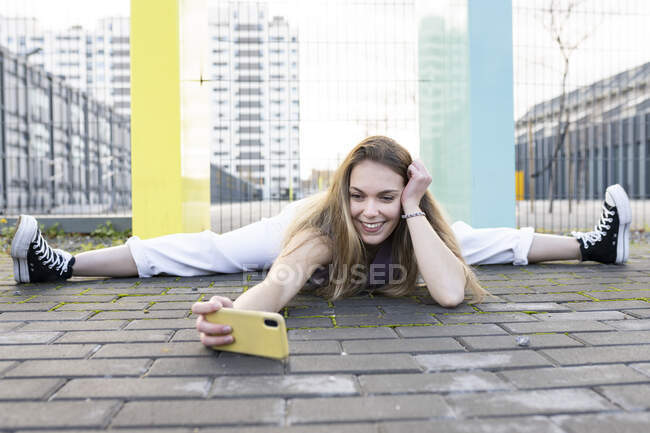 Corpo inteiro feliz ajuste fêmea fazendo rachaduras na calçada pavimentada e tirar selfie no telefone celular no ambiente urbano moderno — Fotografia de Stock