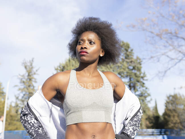 Low angle of confident female runner in sportswear standing at stadium on sunny day during workout and looking away — Stock Photo