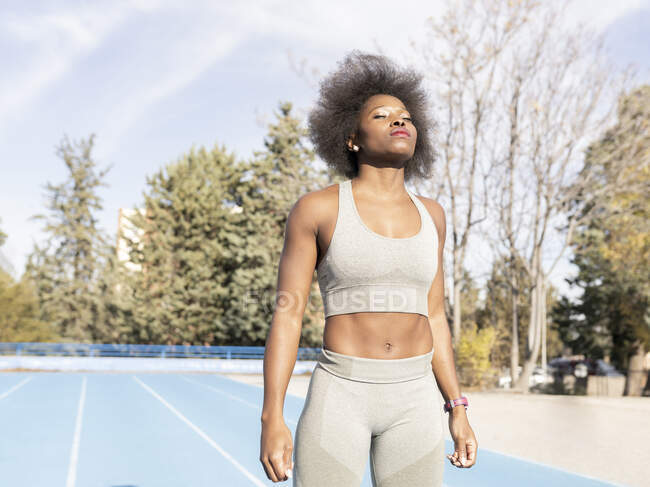 Selbstbewusste Läuferin in Sportbekleidung steht am sonnigen Trainingstag mit geschlossenen Augen im Stadion — Stockfoto