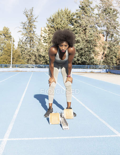 Von unten eine afroamerikanische Läuferin in den Startblöcken, die in geduckter Position steht, während sie sich im Stadion auf den Sprint vorbereitet — Stockfoto