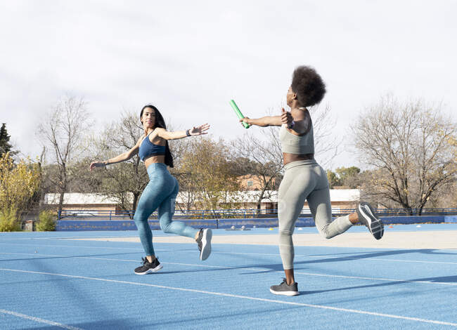 Вмістити багаторасових спортсменів, що проходять повз палицю під час бігу по трасі на стадіоні під час естафети — стокове фото
