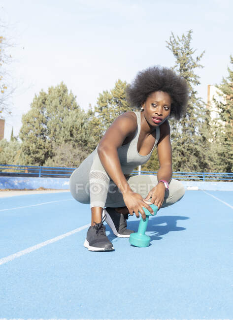 Atleta negra focada fazendo exercícios com haltere enquanto treina no estádio no verão e ansiosa — Fotografia de Stock