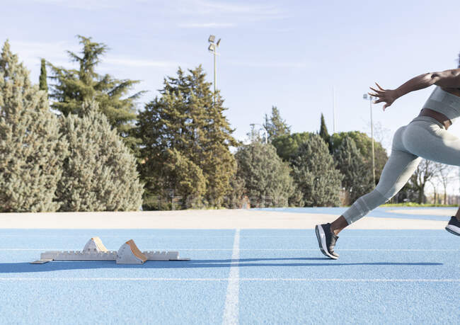 Seitenansicht der energischen afroamerikanischen Athletin, die beim Training im Stadion aus den Startlöchern läuft — Stockfoto