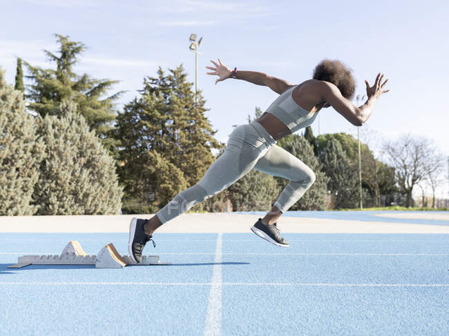 Vue latérale de l'athlète féminine afro-américaine énergique à court de blocs de départ pendant l'entraînement au stade — Photo de stock