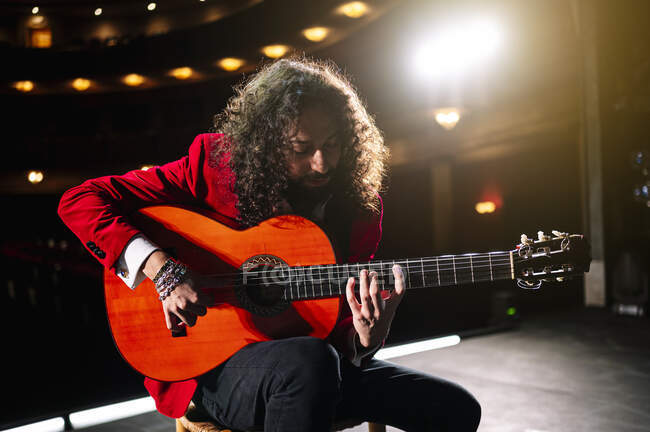 Focused male musician sitting on chair and playing guitar during rehearsal on stage — Stock Photo