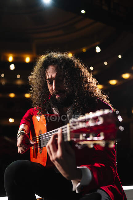 Seitenansicht eines fokussierten männlichen Musikers, der während der Probe auf der Bühne auf einem Stuhl sitzt und Gitarre spielt — Stockfoto
