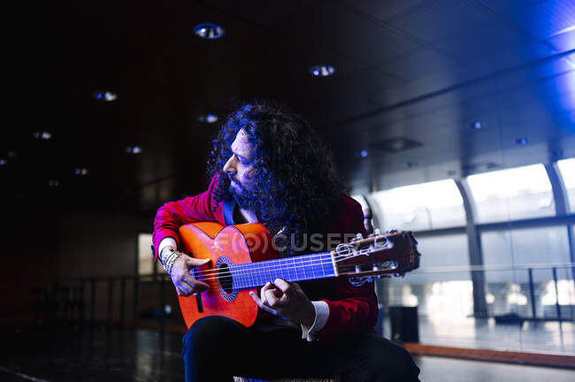 Músico masculino sentado na cadeira e tocando guitarra durante o ensaio no palco — Fotografia de Stock