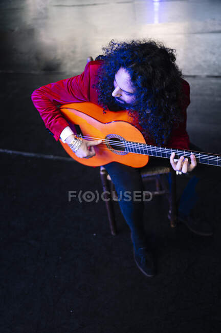 Corpo inteiro de músico masculino focado sentado na cadeira e tocando guitarra durante o ensaio no palco — Fotografia de Stock