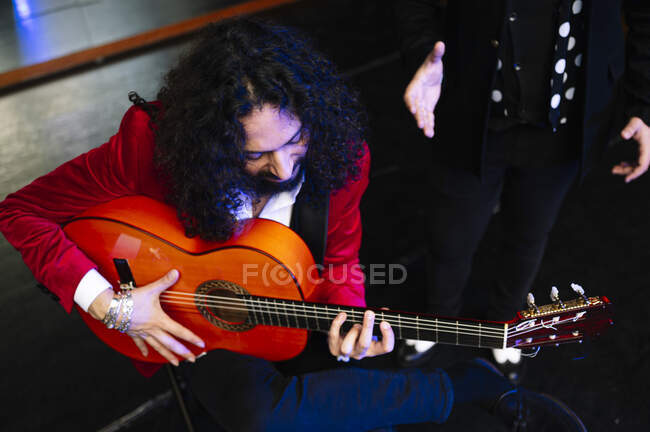 Músico masculino étnico sosteniendo el acorde en las cuerdas de la guitarra mientras toca música con el artista en concierto - foto de stock