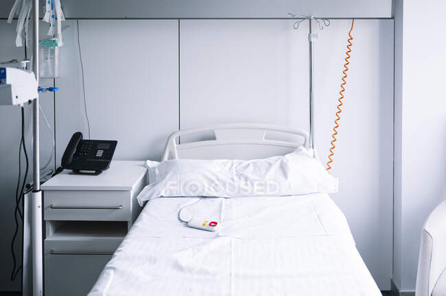 Letto vuoto con pulsante di chiamata infermiera vicino al cavalletto IV in reparto luce attrezzato in ospedale contemporaneo — Foto stock