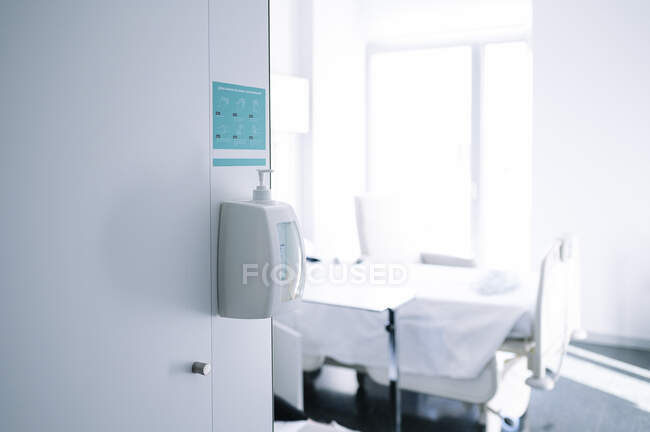 Интерьер светлой пустой палаты с постелью и дезинфицирующим средством для рук в современной оборудованной больнице — стоковое фото